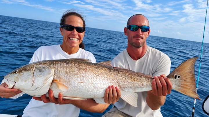 Two anglers holding a large red drum.