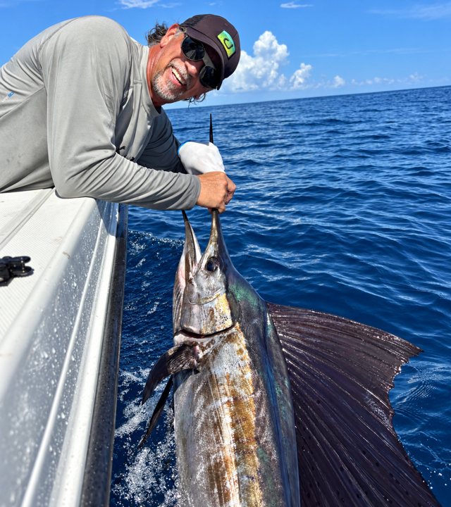 Angler beside a sailfish in the water.