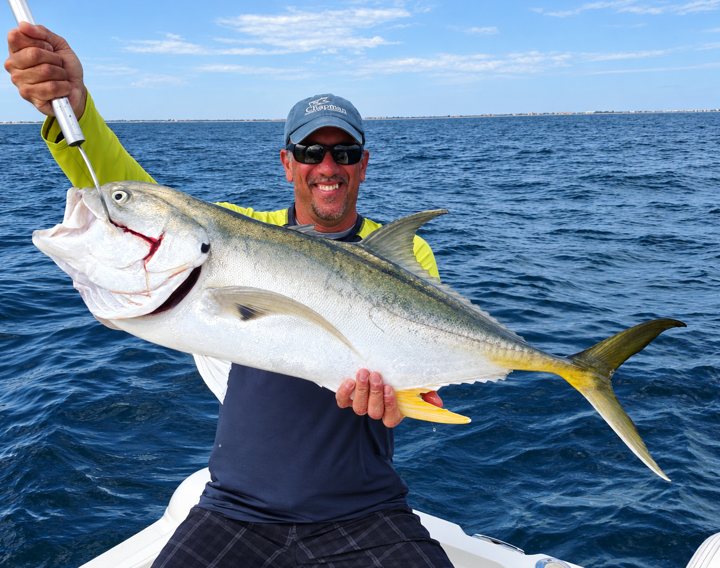 Angler holding a large silver fish against the blue ocean.