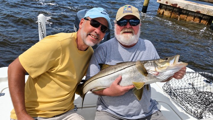 Two anglers holding a snook aboard a fishing boat.